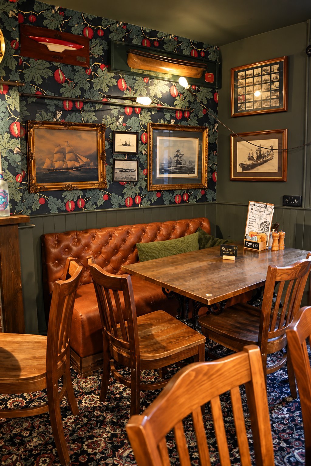 Cozy dining nook with wooden chairs, leather banquette, and ship paintings and nautical decor on dark walls