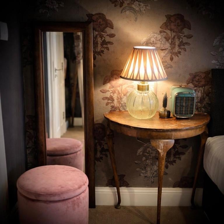 A Union Inn bedroom corner with a wooden vanity table, a pleated lamp shade, pink velvet ottoman and an ornate mirror