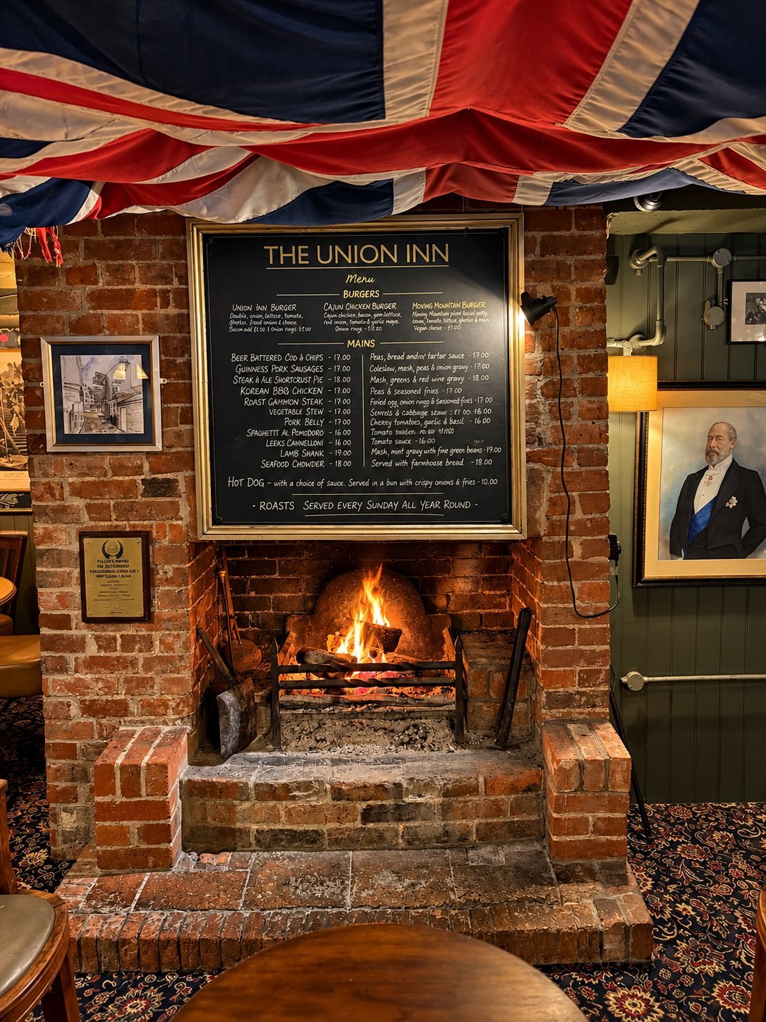 The Union Inn fireplace with a burning log fire, a chalked menu board mounted above, the Union Jack bunting overhead, and a vintage portrait to the side