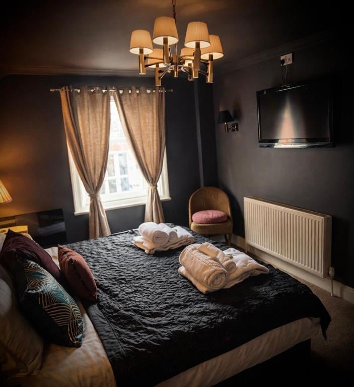 An elegant Union Inn bedroom with dark walls, a gold chandelier, black bedding and a wall-mounted TV