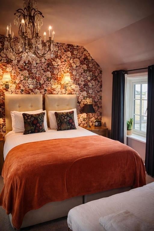 A Union Inn bedroom with ornate floral wallpaper, an upholstered headboard and a crystal chandelier