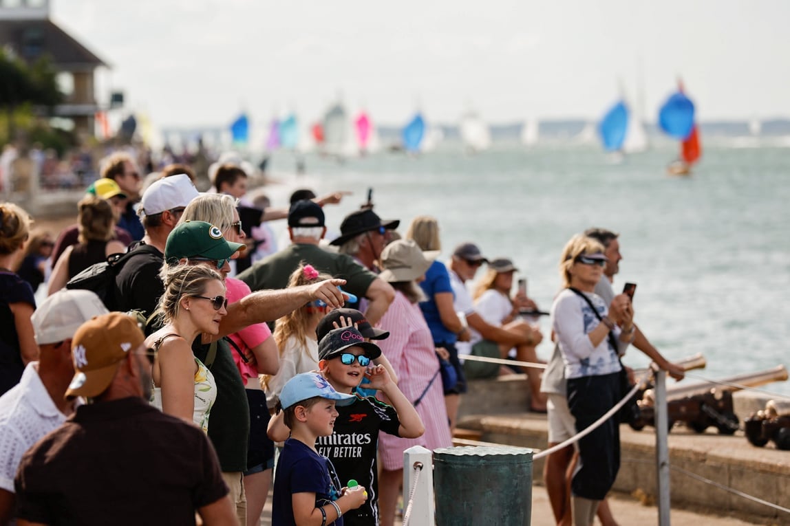 Crowd of spectators watching sailboats from a waterfront dock on a sunny day