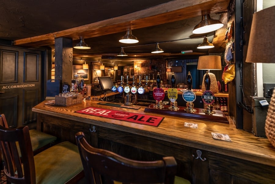 Interior of a rustic bar with wooden counter, vintage lighting, bottles on shelves, and a red sale sign