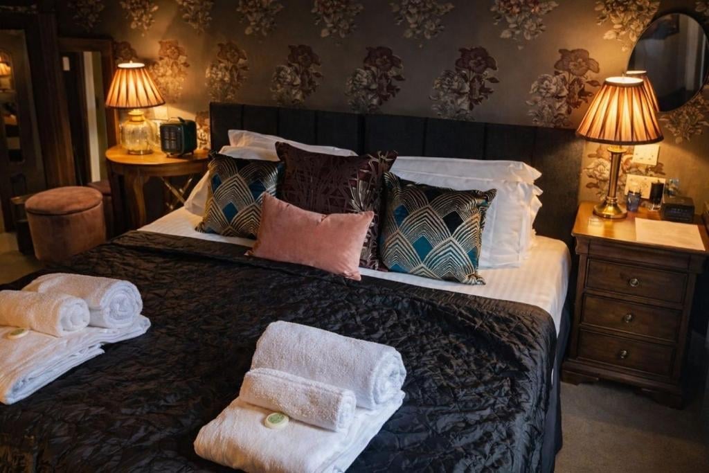 A luxury Union Inn bedroom with a black bed, decorative pillows, rolled white towels and warm gold lamps
