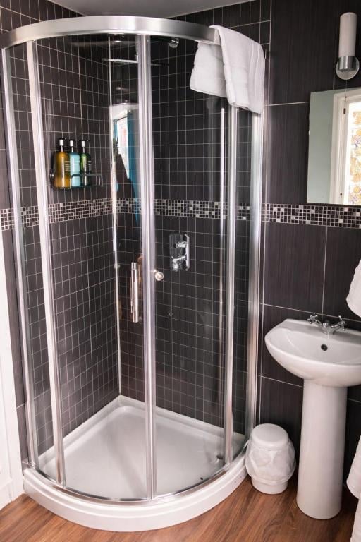 A modern black tiled shower enclosure with curved glass doors and a pedestal sink in a Union Inn bathroom